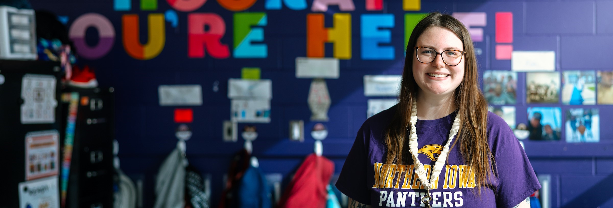 Female student with long brown hair in front of colorful classroom wall