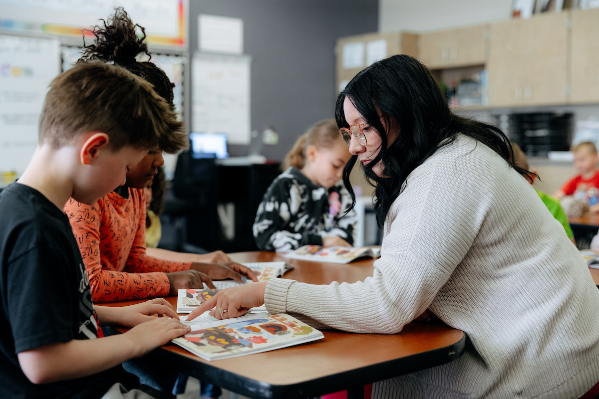 Student working with elementary students and books at table