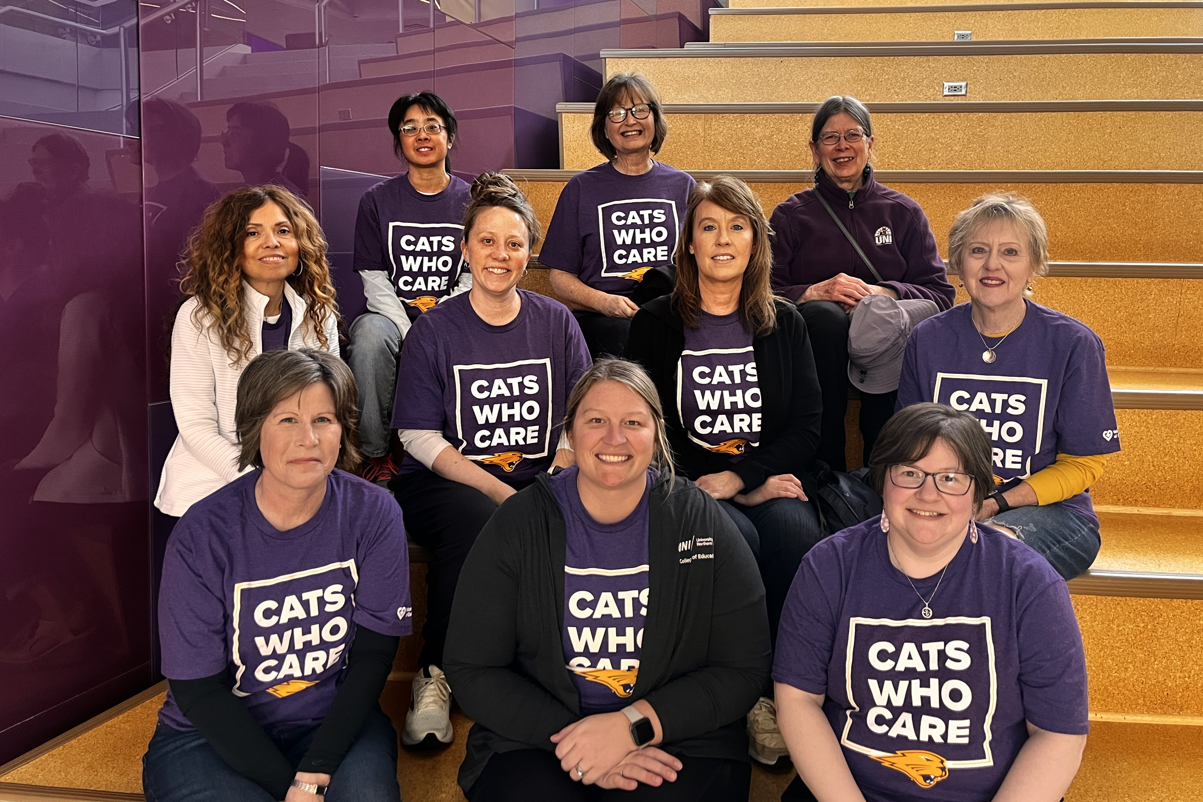College faculty and staff in Cats Who Care T-shirts on stairs in Schindler Education Center