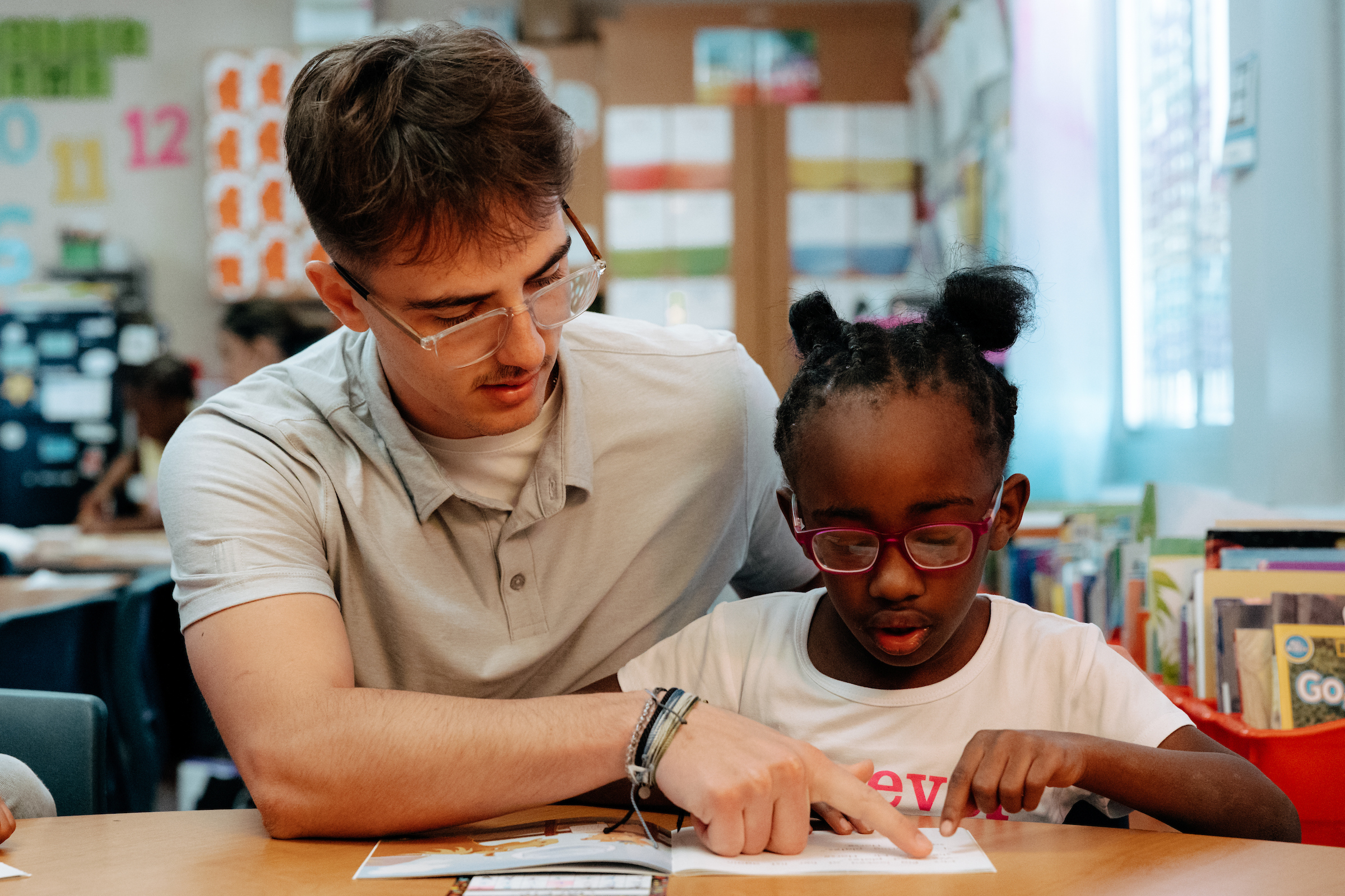 Elementary student teacher with student reading at desk 